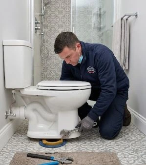 Toilet repair technician inspecting base leak, wax ring, and water connection in Montreal
